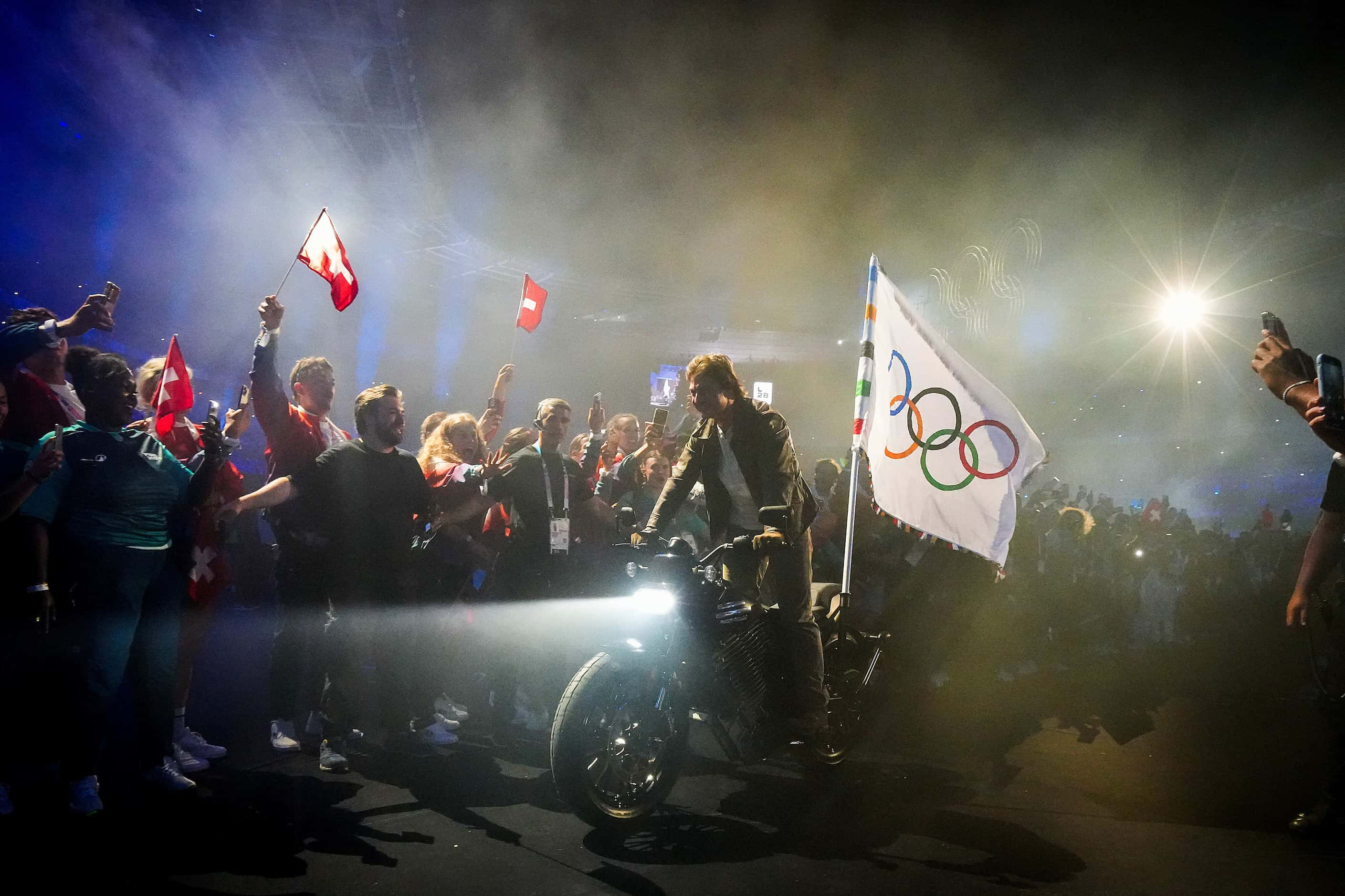 Actor Tom Cruise rides through athletes on a motorcycle carrying the Olympic flag after a...