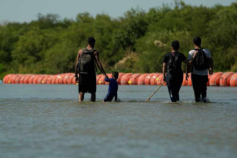 Migrants crossing into the U.S. from Mexico walk along large buoys being used as a floating...