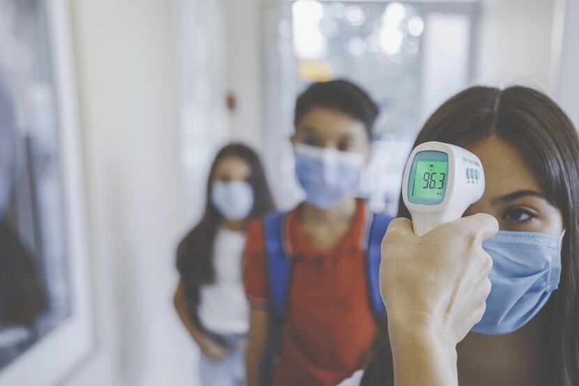 Young female student wearing a mask has her temperature checked before attending school.