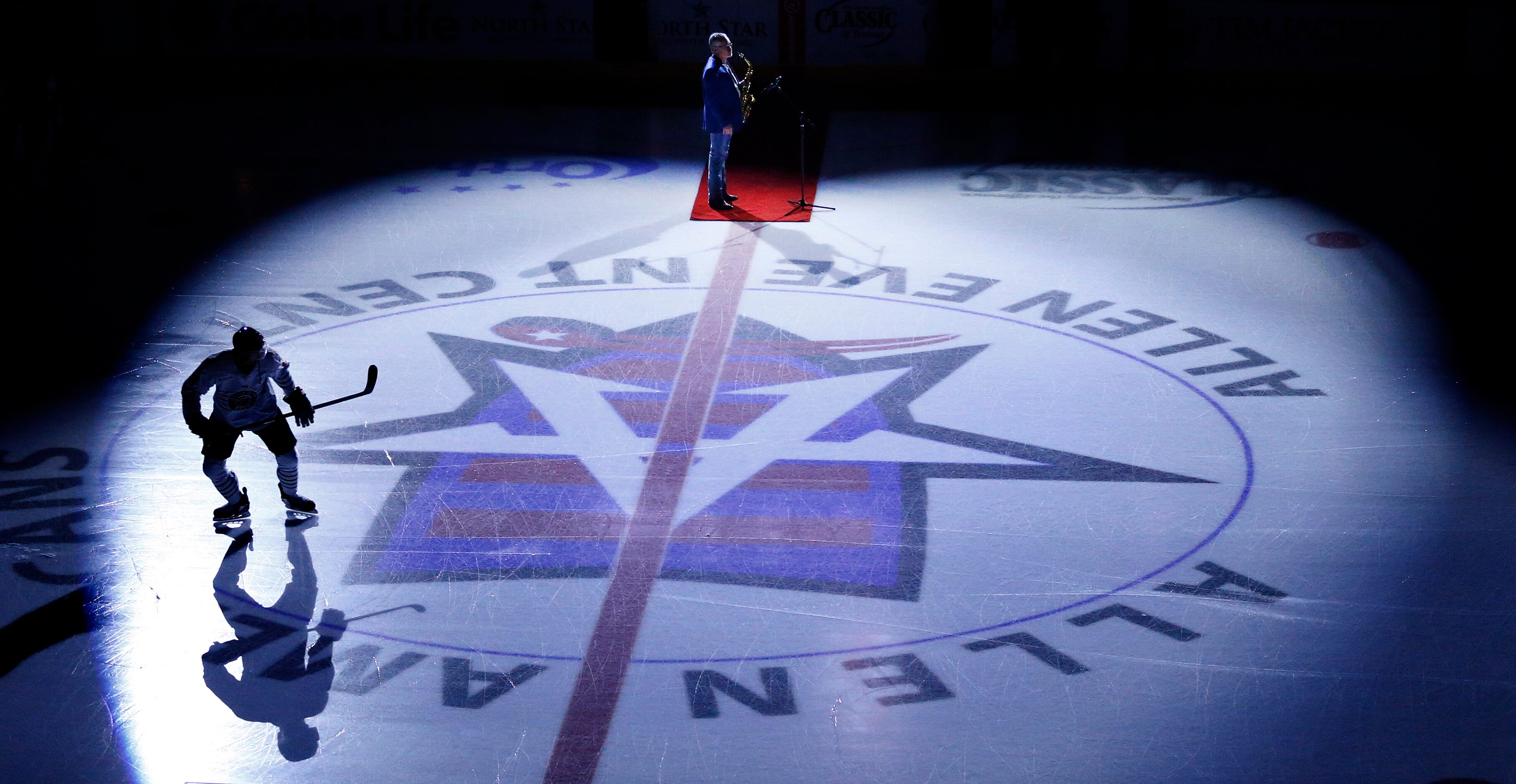 A Rapid City Rush hockey player takes the ice under the spotlights as a saxophonist prepares...