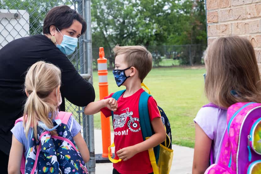 Administrative assistant Erin Johnston, left, gives an elbow bump to kindergarten student...