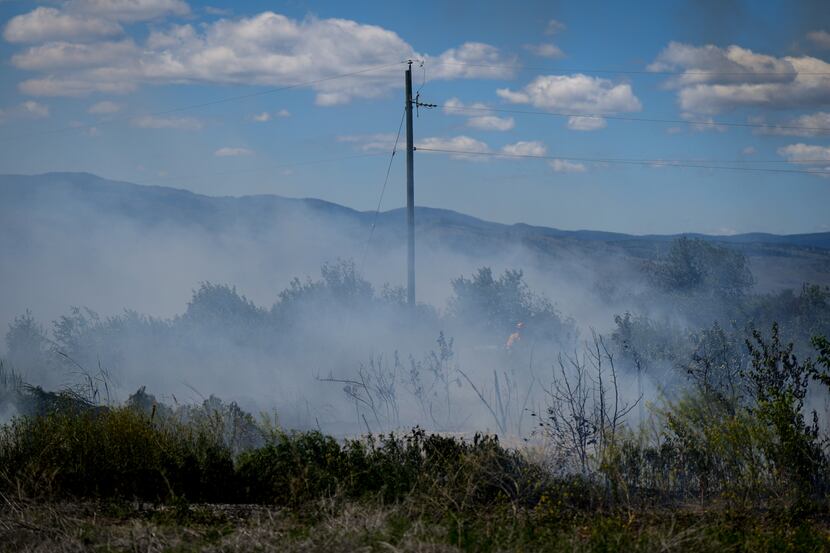 A firefighter directs water on a grass fire on an acreage behind a residential property in...