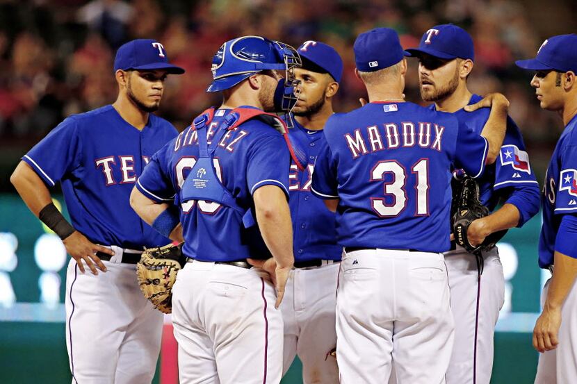 Players look on as Texas Rangers pitching coach Mike Maddux (31) tries to calm relief...