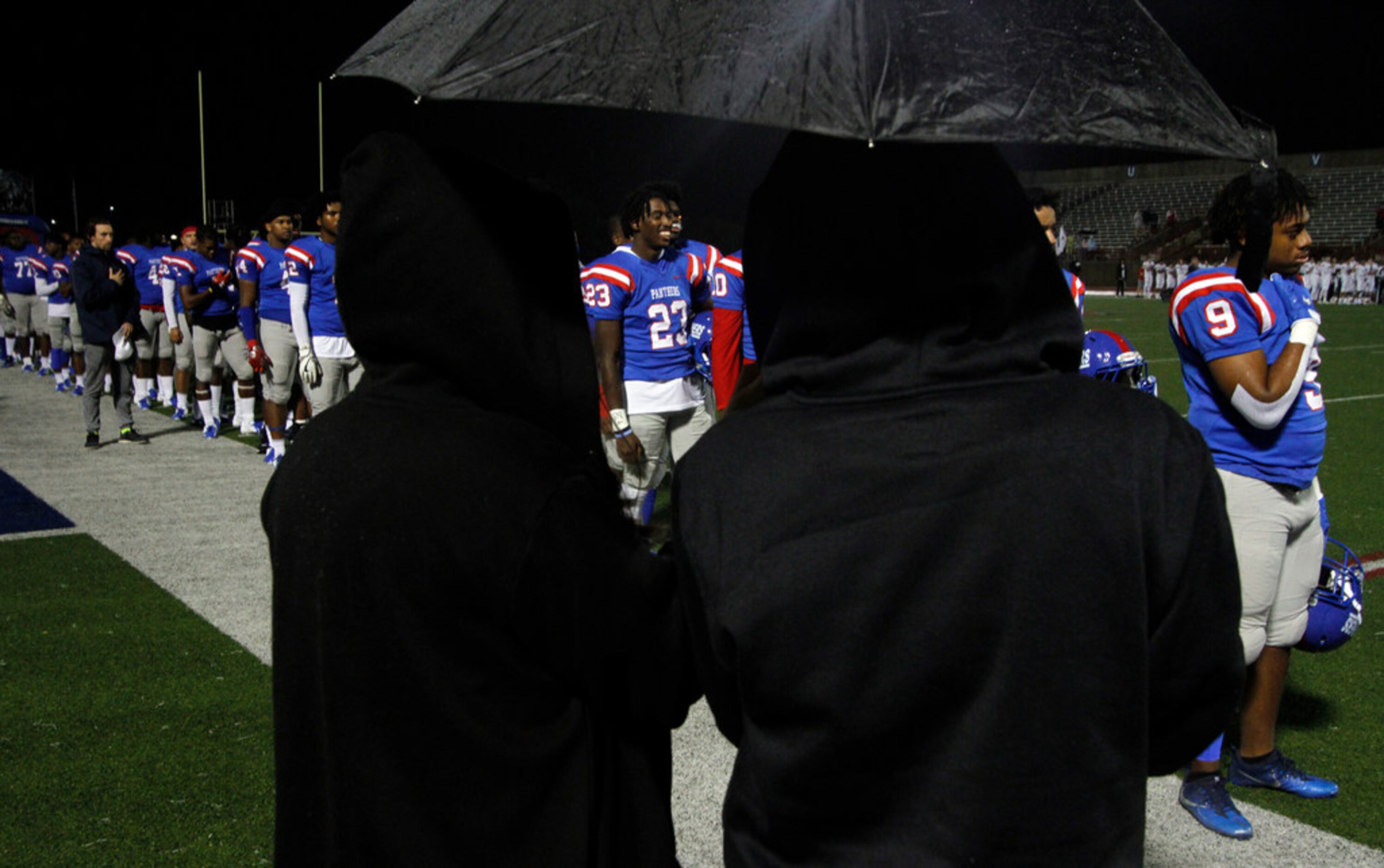 A couple of student photographers stay dry under an umbrella as they photograph Duncanville...