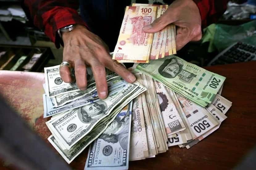 Un empleado de una casa de cambio entrega dólares estadounidenses y pesos mexicanos enviados...