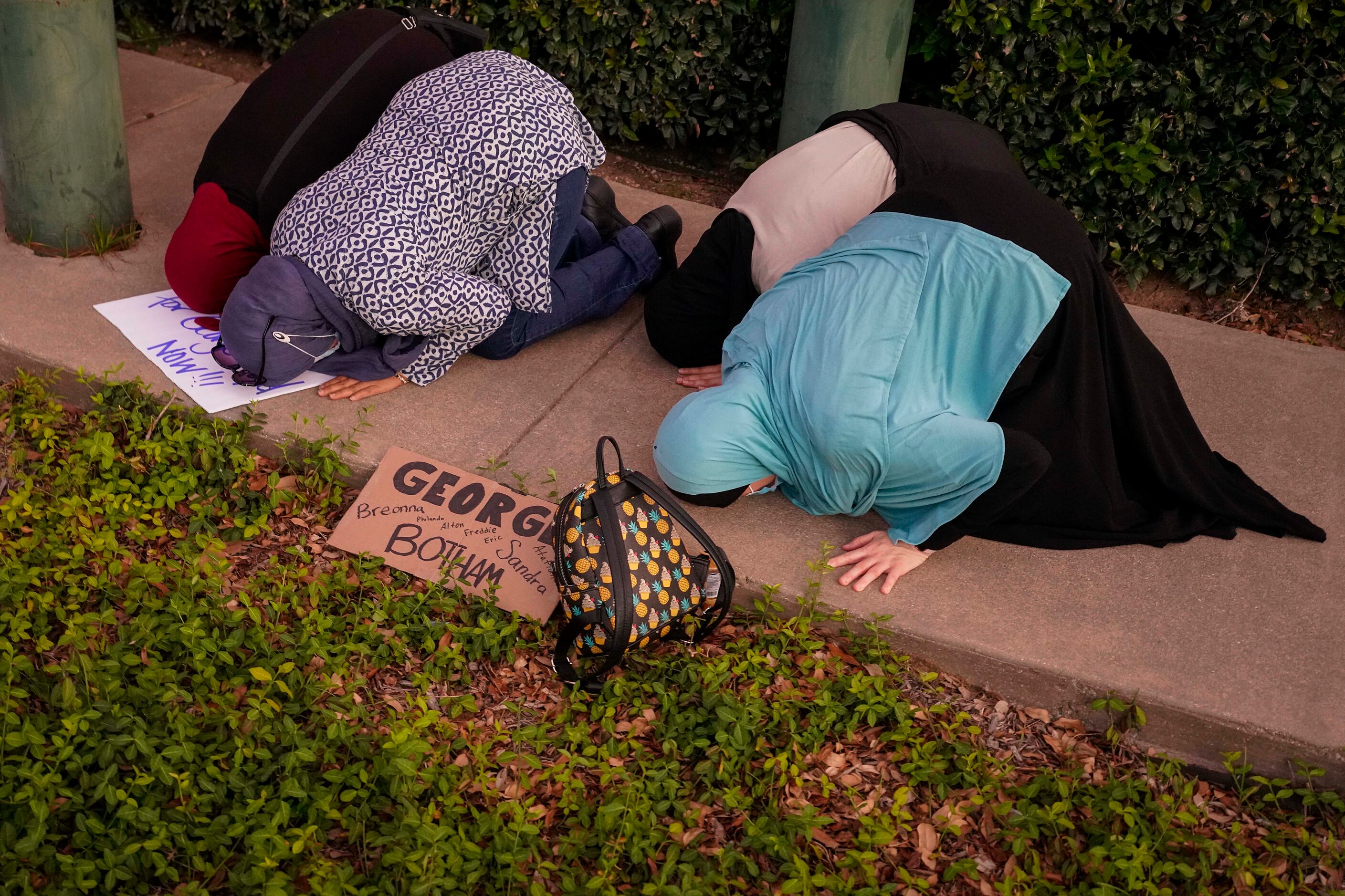 A group of muslim women steps aside from the crowd and puts down their protest signs to...