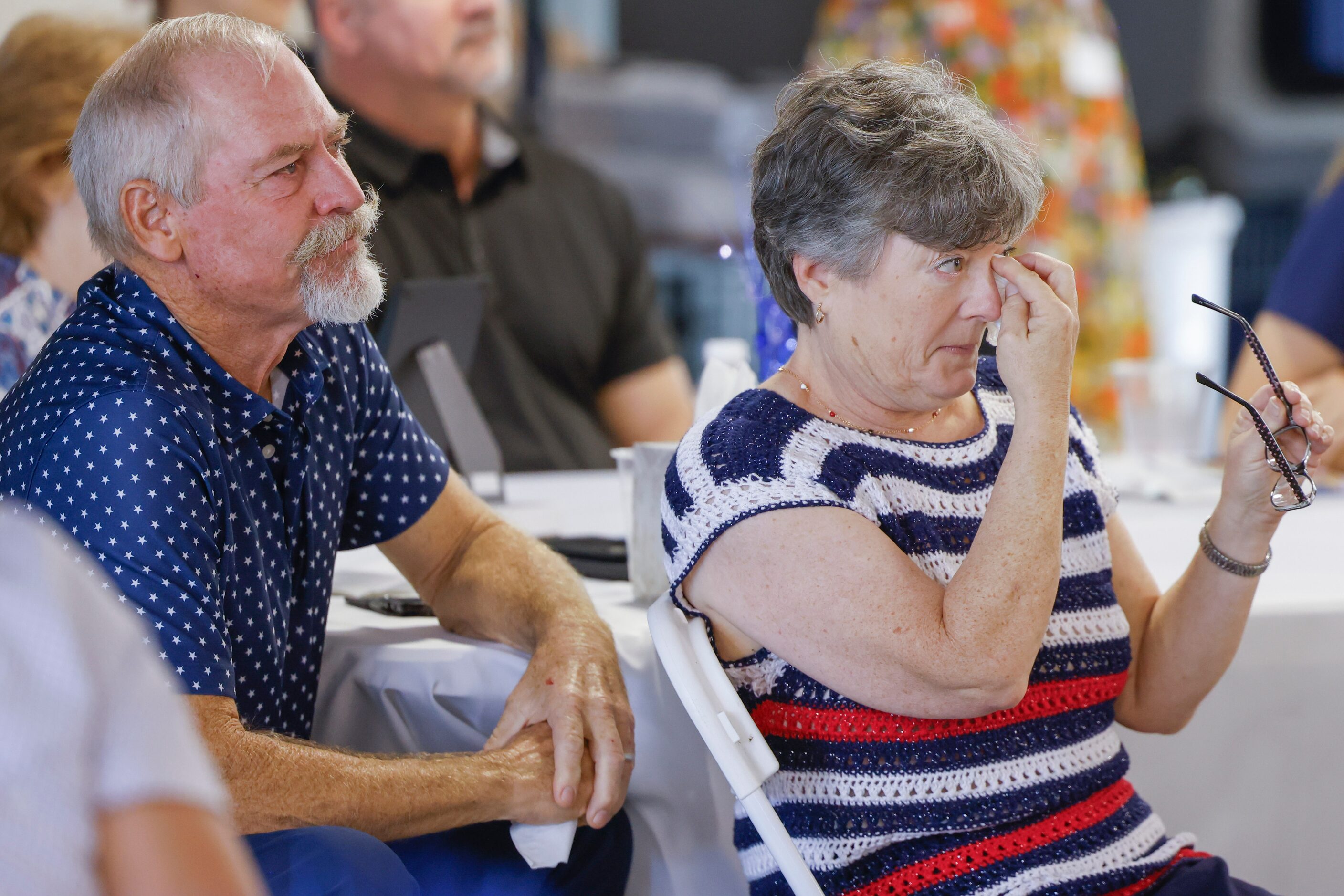 Veteran Kathy Schneider wipes off a tear alongside her husband Ray while watching a video...