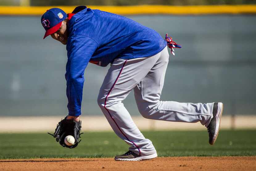 Texas Rangers shortstop Elvis Andrus fields a ground ball as Ike Davis looks on while...