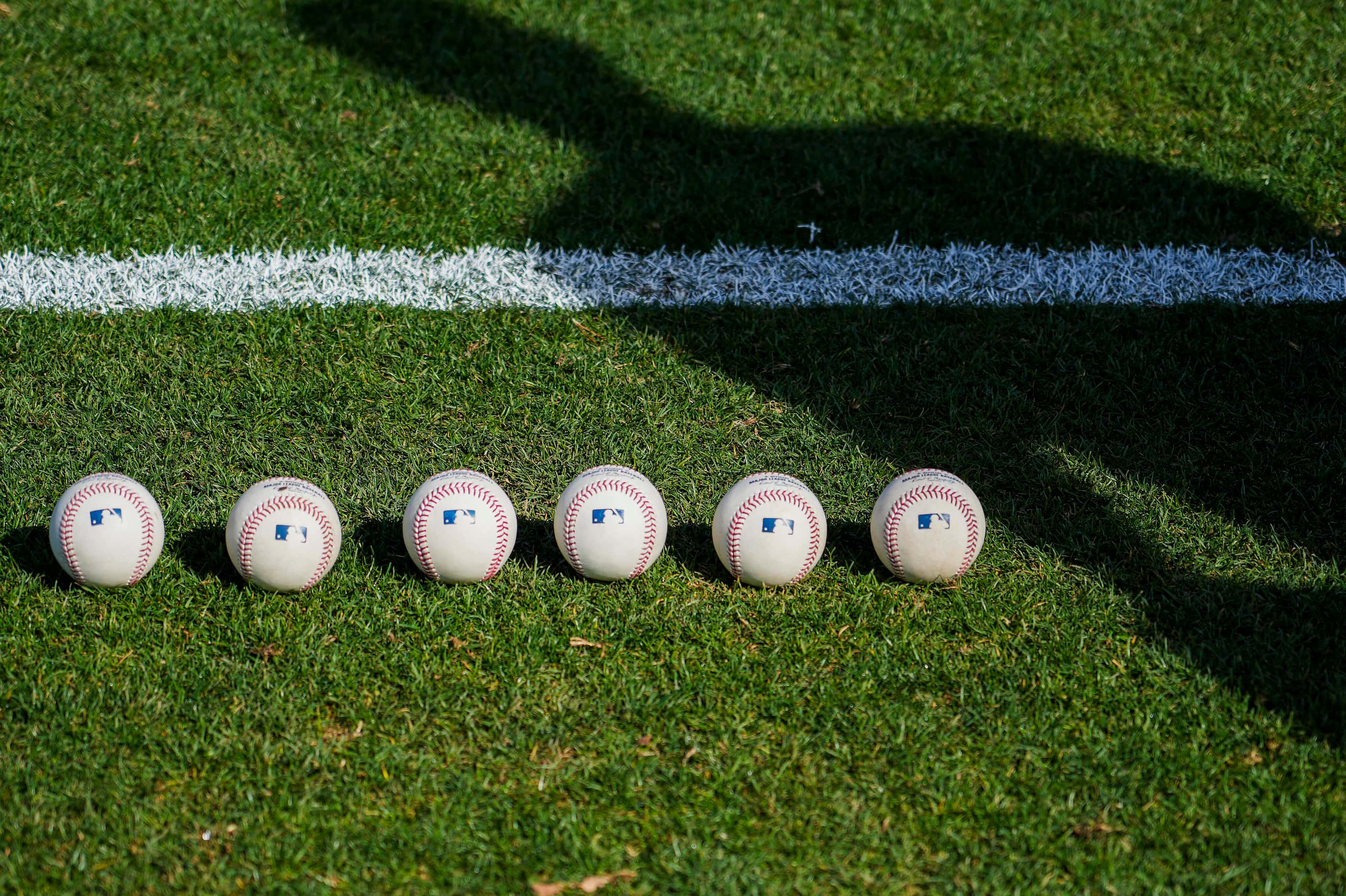 Texas Rangers catcher Sam Huff casts a shadow over balls laid out in the outfield before a...