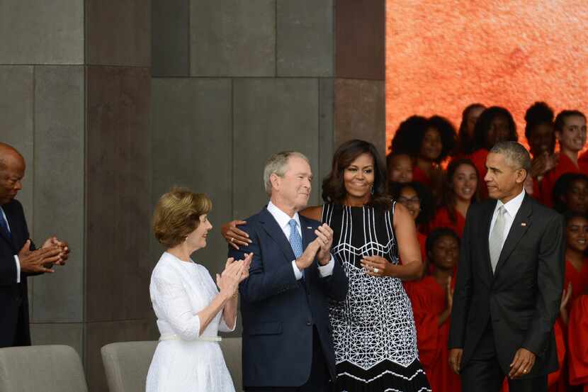 President Barack Obama watches first lady Michelle Obama embracing former president George...
