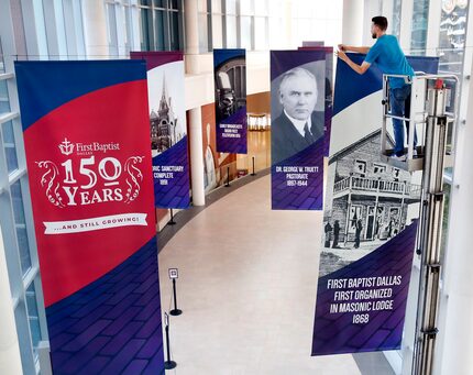 Building technician Micah Lynch hangs banners along an indoor walkway in advance of First...