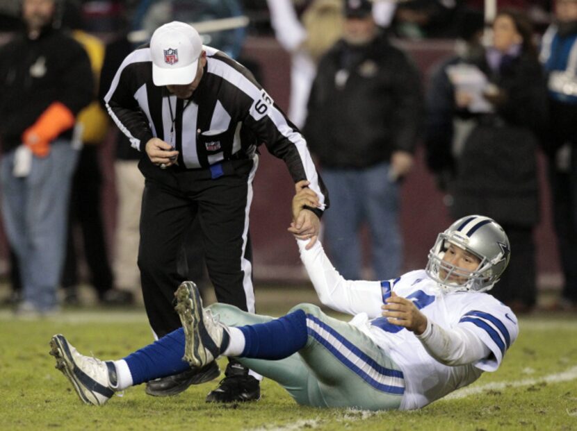 Dallas Cowboys quarterback Tony Romo (9) is helped up by referee Walt Anderson (66) during...