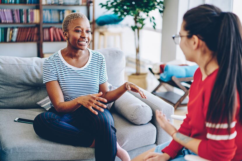 A cheerful woman speaks with a friend while sitting on a couch.