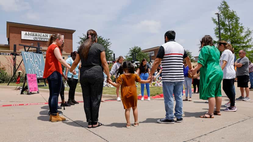 FILE - People hold hands as they pray at a memorial for victims of the Allen Premium Outlets...