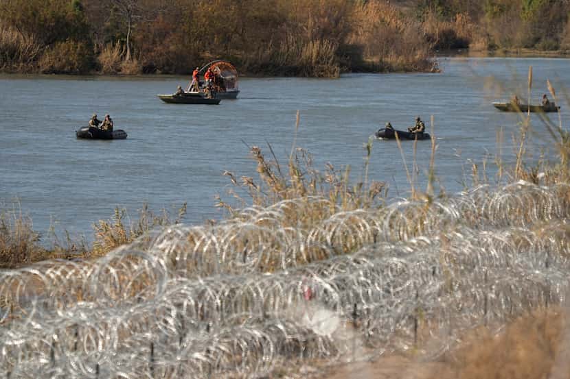 Guardsmen move along the Rio Grande in small boats past rows of concertina wire placed to...