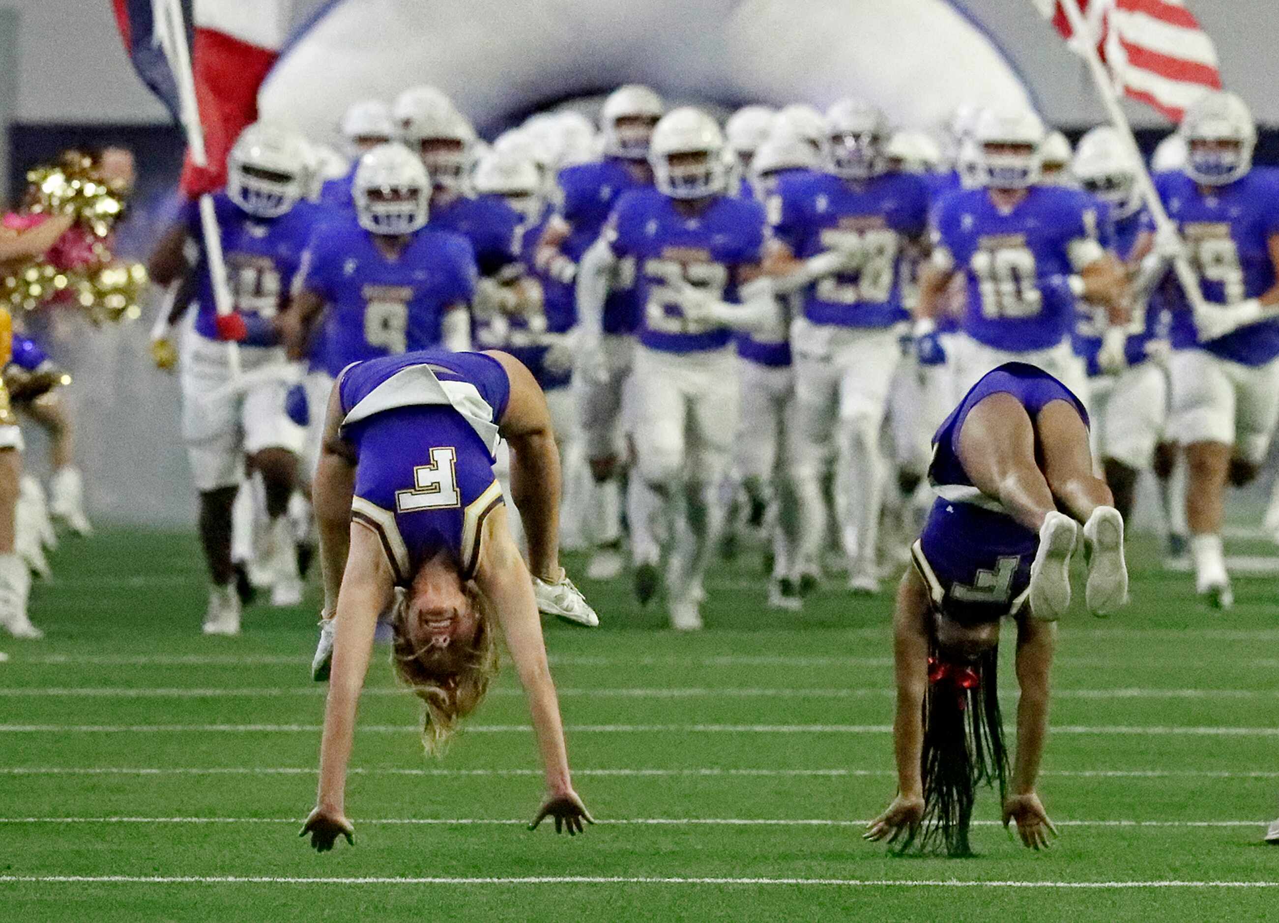 Cheerleaders lead the Frisco High School football team onto the field before kickoff as...