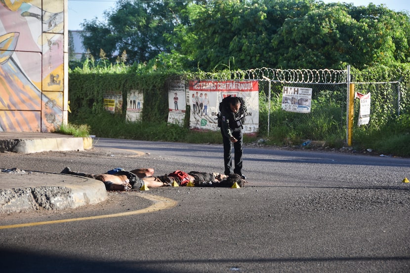 Un oficial de policía toma una fotografía de la escena del crimen en donde se ve cuerpos...