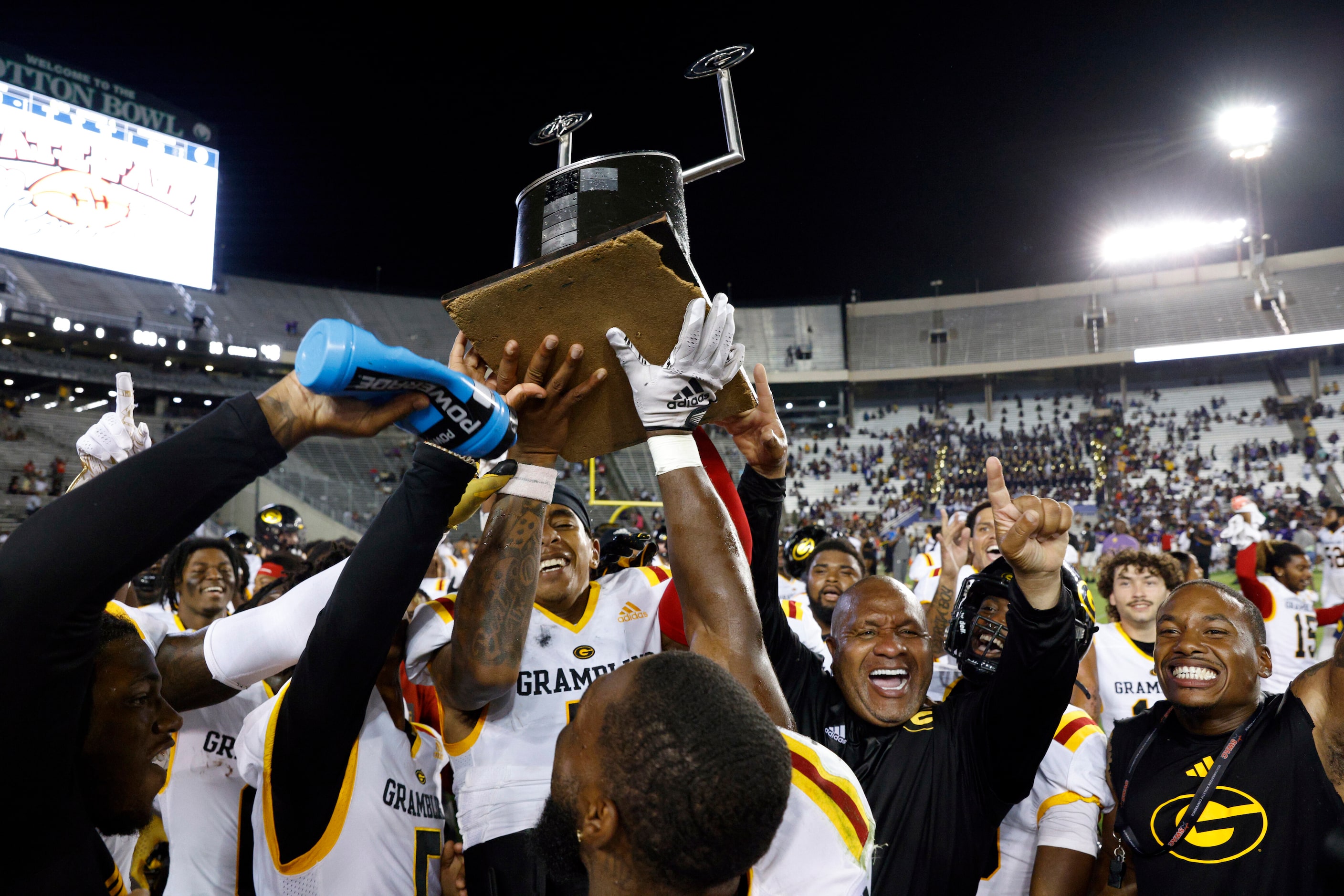 Grambling State head coach Hue Jackson (center right) raises the State Fair Classic trophy...