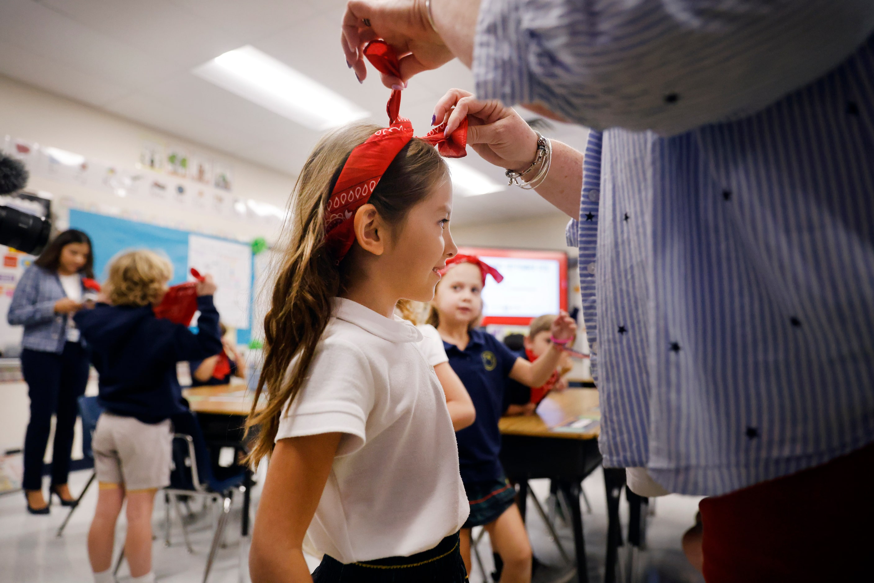 Second grade teacher Stephanie Wellman ties a red handkerchief around Izzy Faiola in honor...