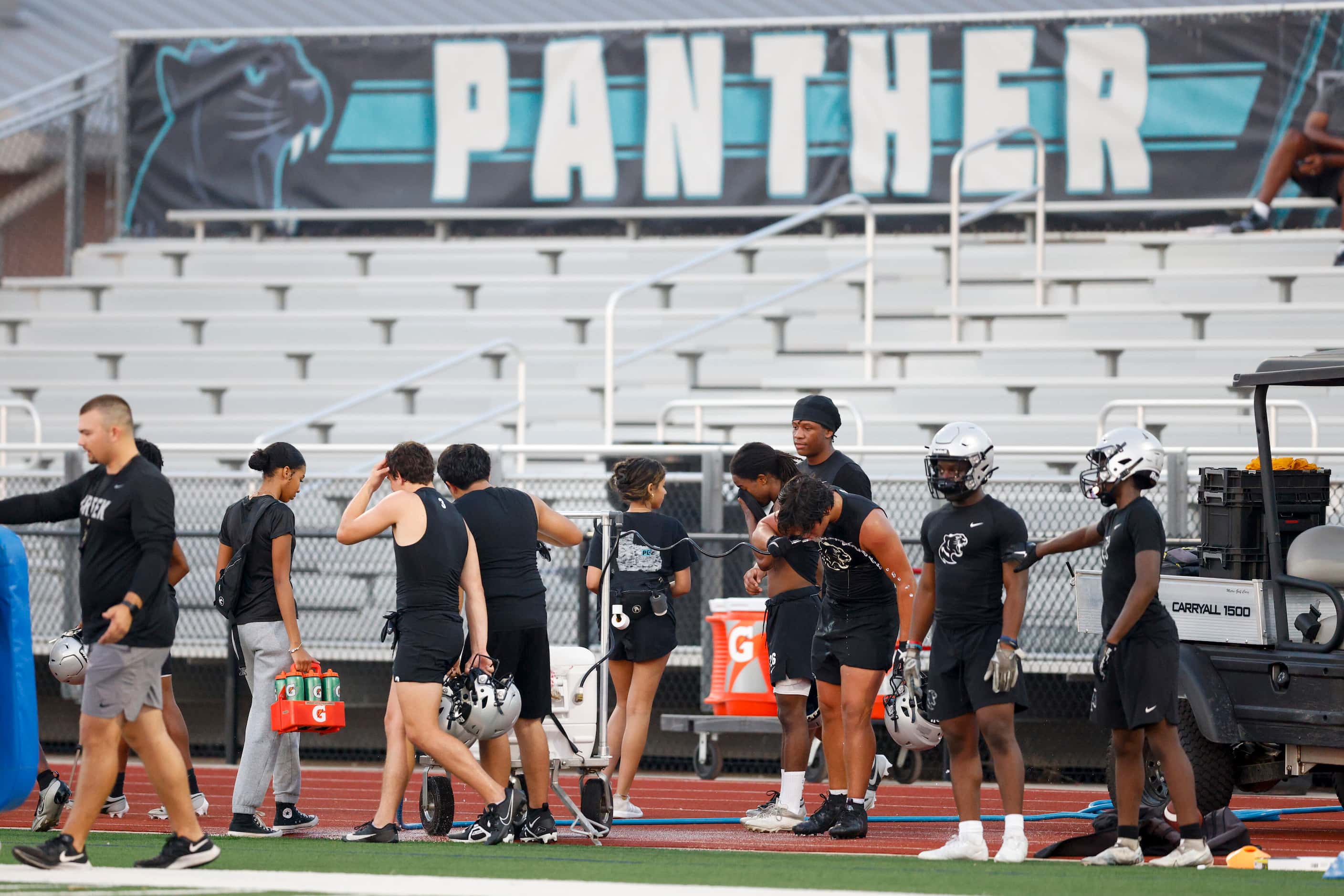Football players drink water during an early morning practice at Panther Creek High School,...