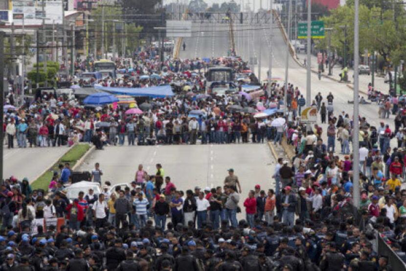 Striking teachers stand in front of a police, below, near the Benito Juarez International...