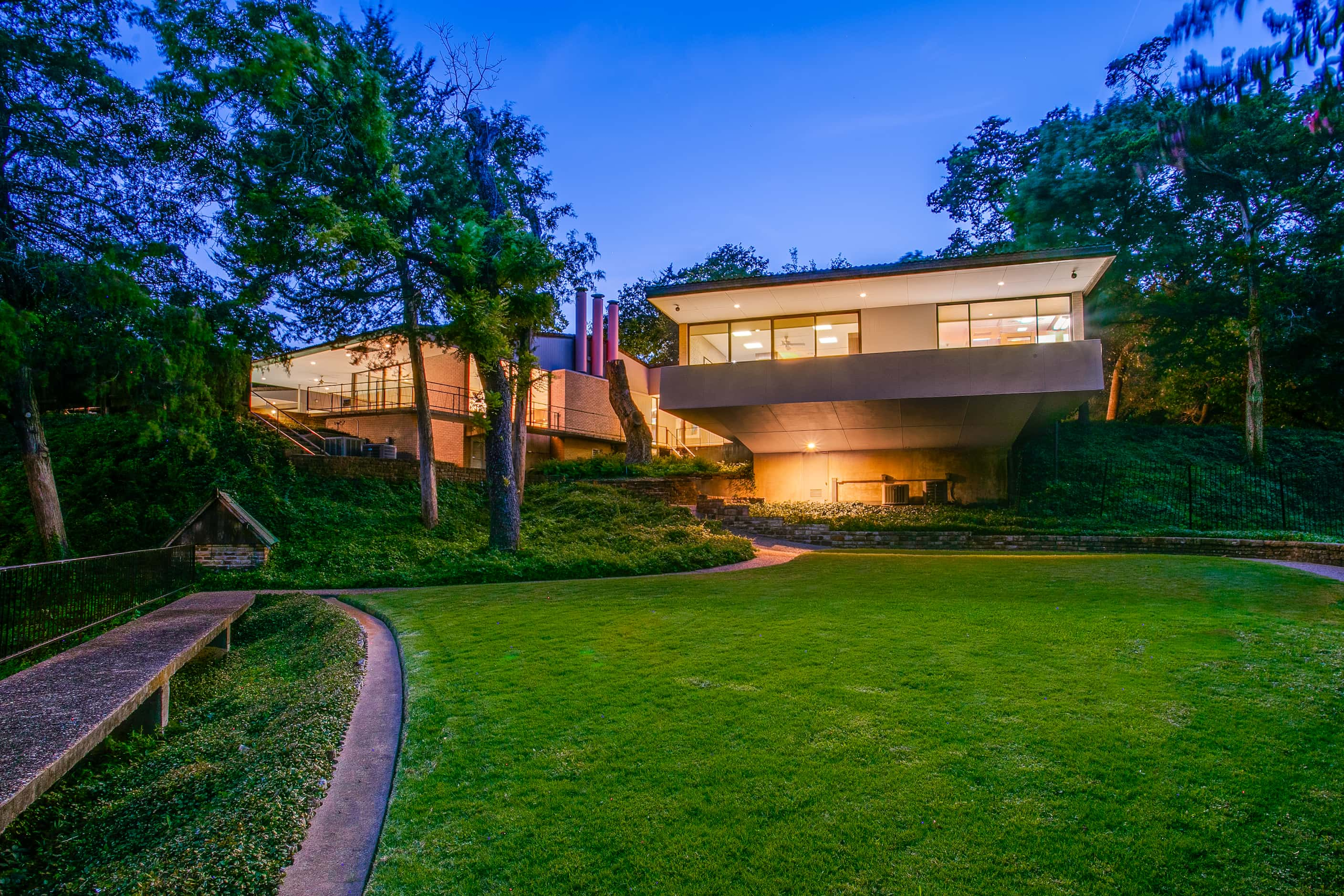 Midcentury modern house viewed at sunset, large area of grass to the back of the house.