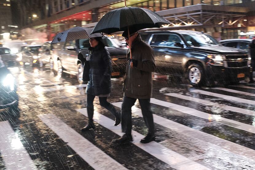 Pedestrians walk through a wintery mix of snow, rain and ice during the evening commute in...
