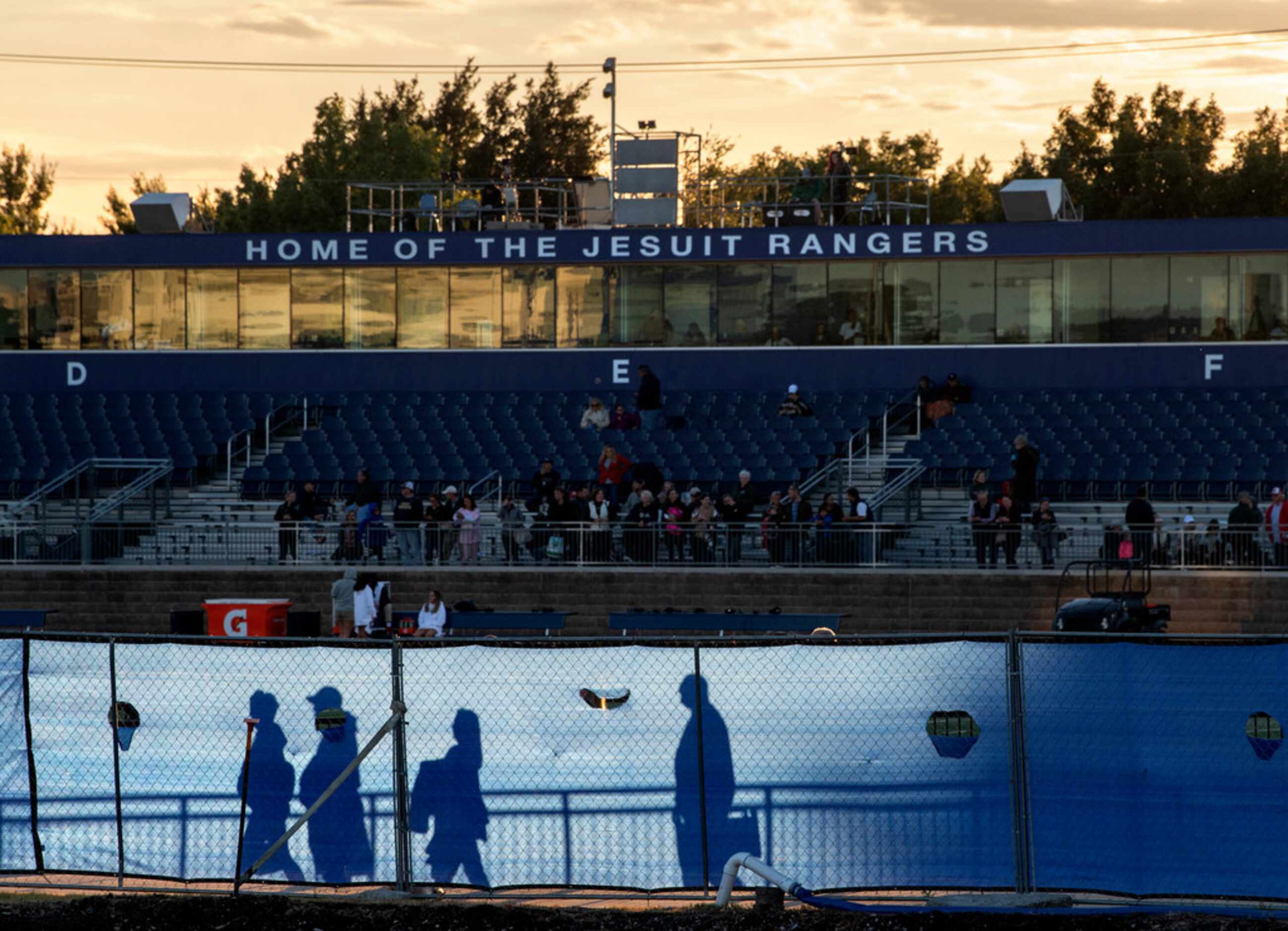 Fans are silhouetted against a construction fence as they enter Postell Stadium for a high...