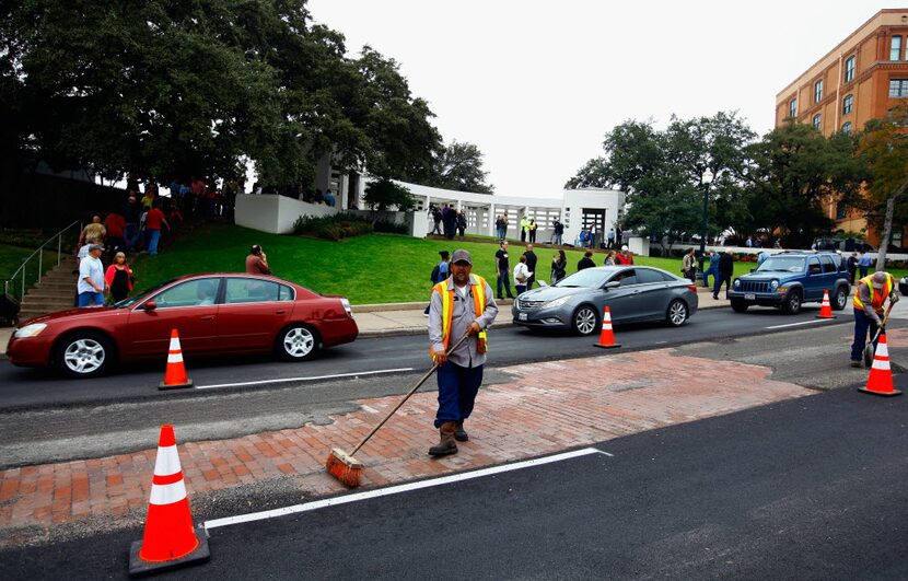  Dallas city workers repair the asphalt on Elm Street in Dealey Plaza as people visit Dealey...