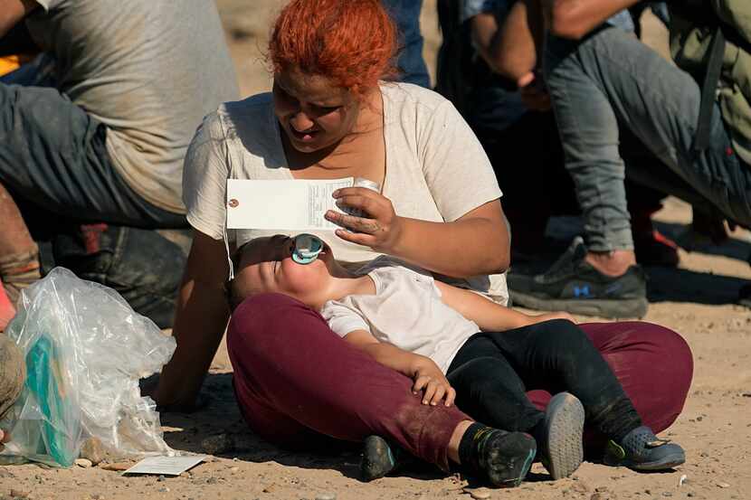 woman shields her child from the sun as she and other migrants wait to be processed by the...