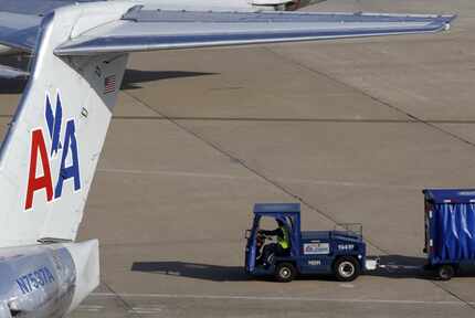 An employee drives with a baggage cart behind an American Airlines jet at DFW Airport.