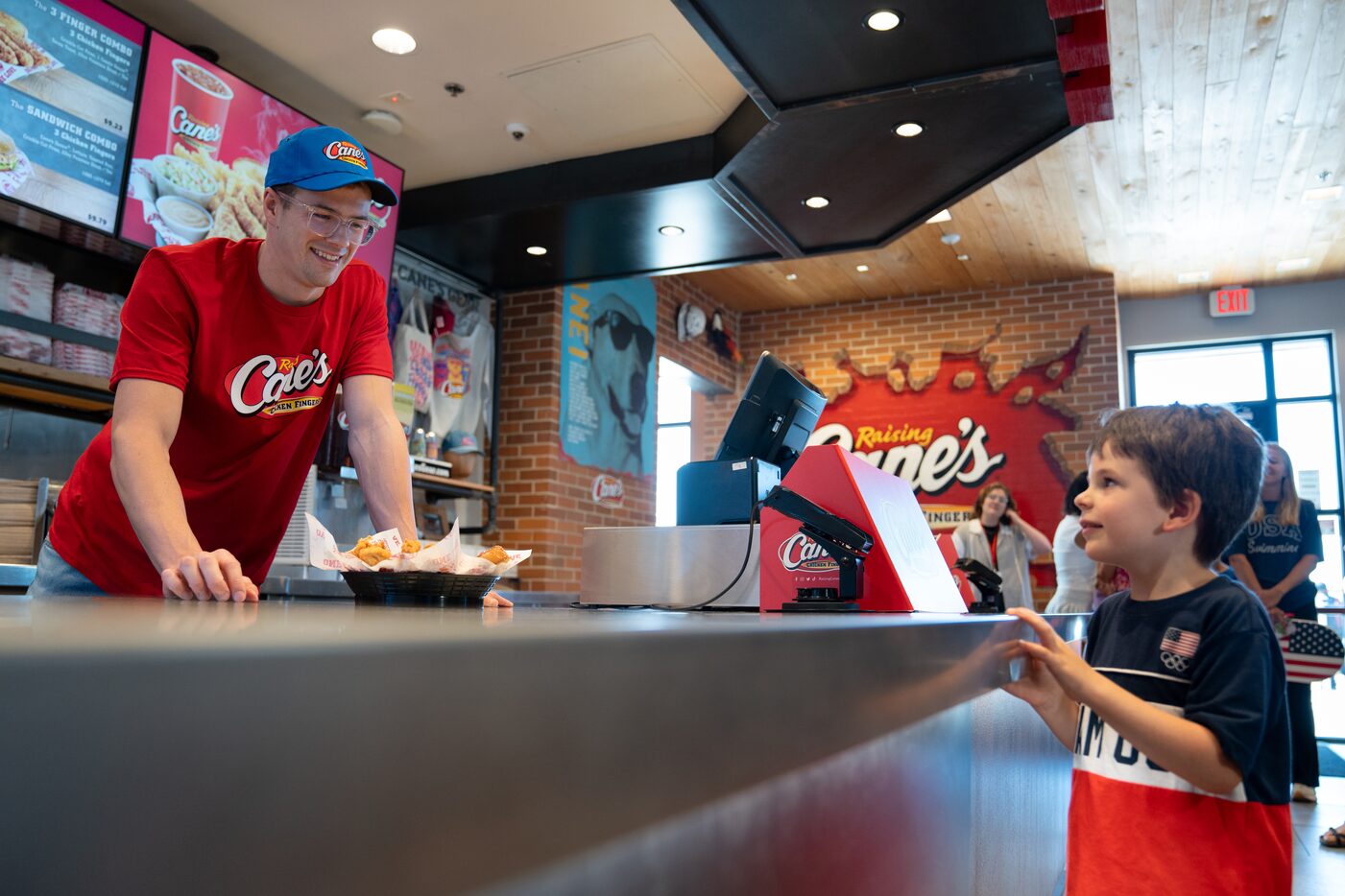 Dallas-based Olympic swimmer Nic Fink hands Wilson Patton, 4, his order at Raising Cane’s in...