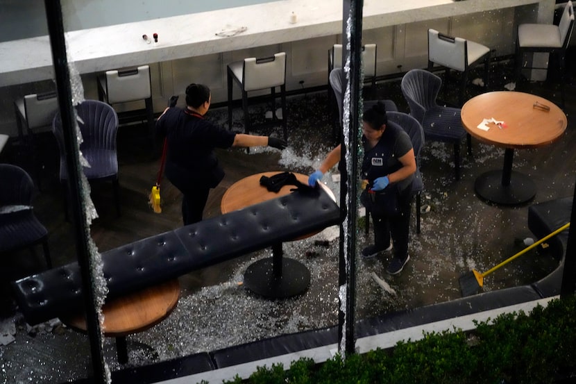 Workers clean up broken glass inside a damaged downtown restaurant after a severe...