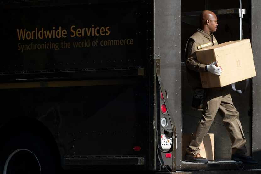 A United Parcel Service (UPS) delivery man unloads boxes from his truck outside a business...
