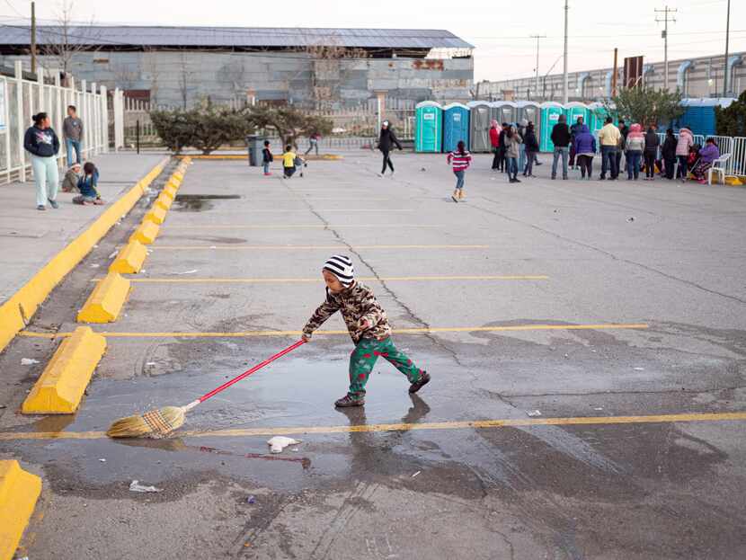 A young migrant plays with a broom in a puddle at the state run migrant shelter in Juarez.