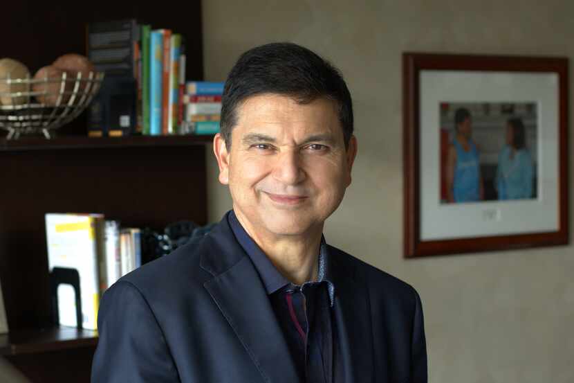 Man in navy suit jacket smiles at camera with bookshelves in background.