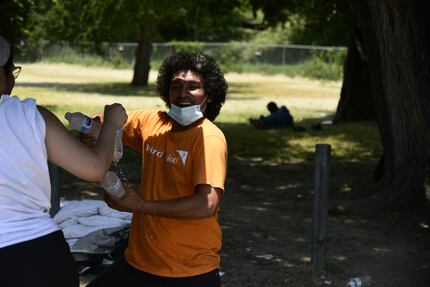 Volunteer Shelly Flores hands Carlos Pena water bottles provided by Feed the People Dallas...