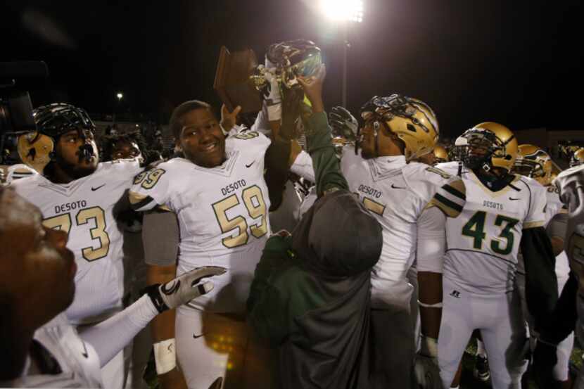 A young boy holds up the game trophy, as the DeSoto team, including D'ozhane Williams (73);...