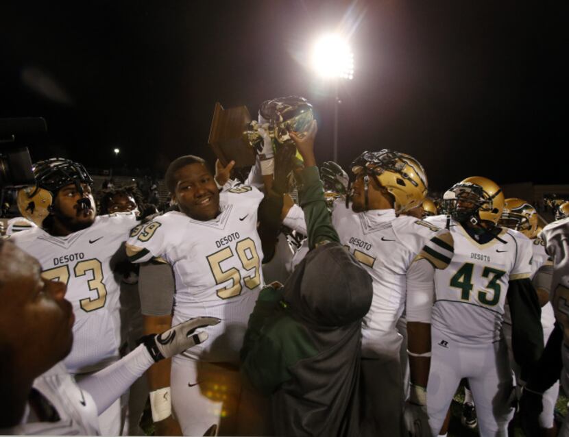 A young boy holds up the game trophy, as the DeSoto team, including D'ozhane Williams (73);...