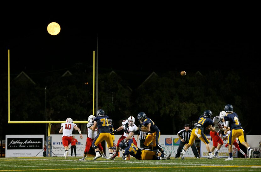 The moon rises behind Highland Park quarterback John Stephen Jones' (9, right) pass in the...