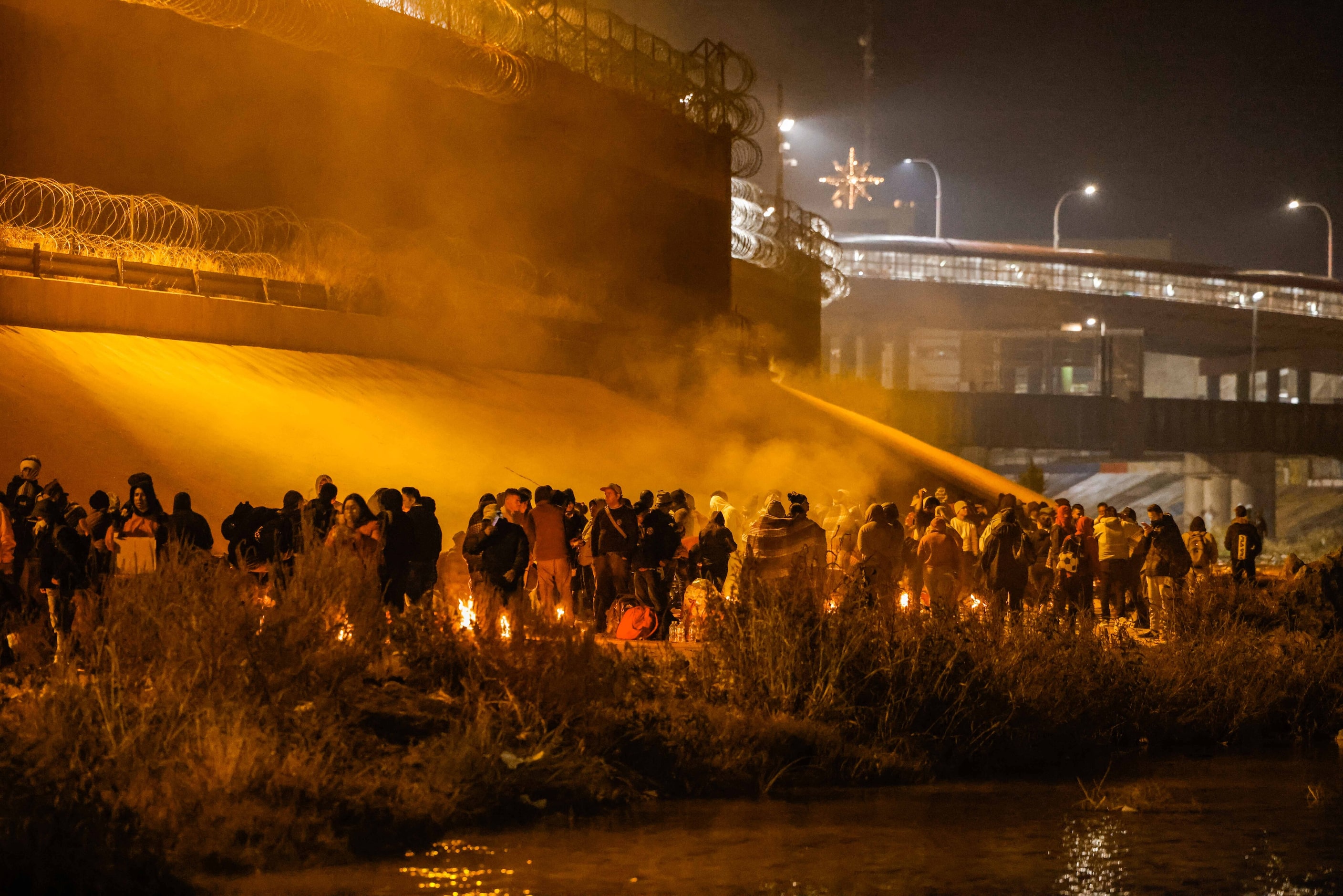 Migrants wait in line along a border wall in El Paso, Texas after crossing the Rio Grande...