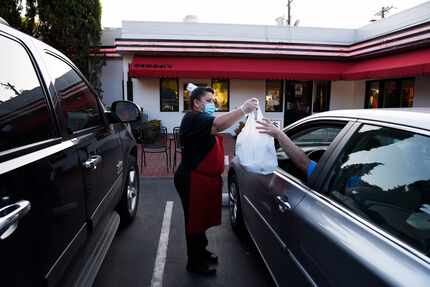 Claudia Beltran, center, hands a food order to a customer at the curbside parking outside of...