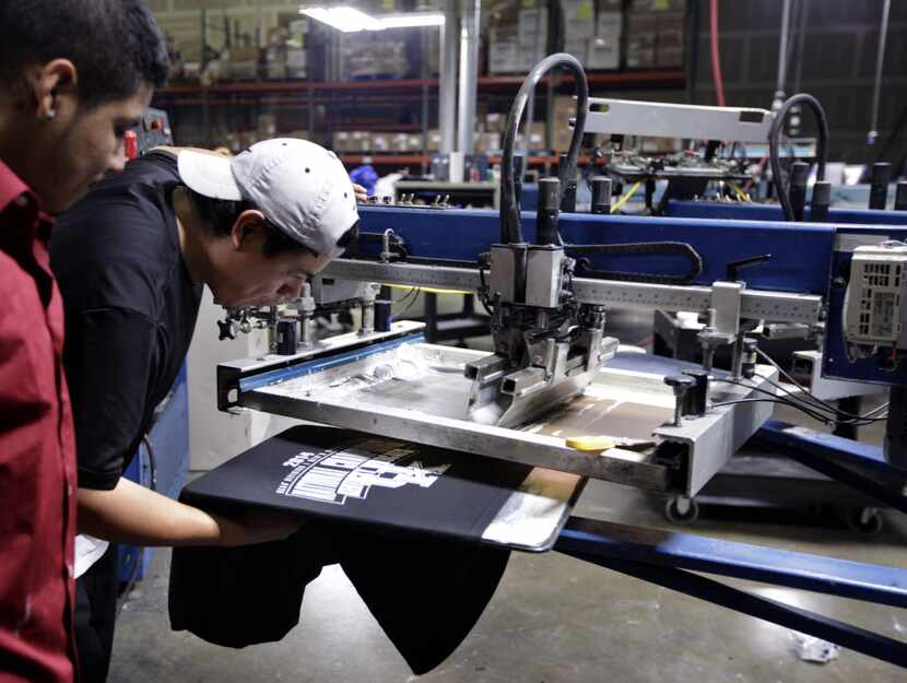 Alex Cruz, left, and Nery Herrera check a sample NCAA championship t-shirts for defects at...