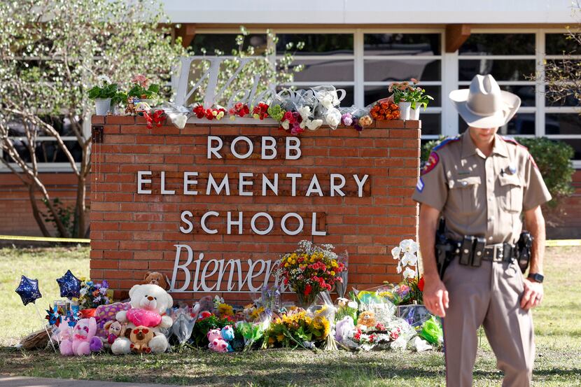 A Texas state trooper stands near a sign with flowers and balloons in memory of those killed...