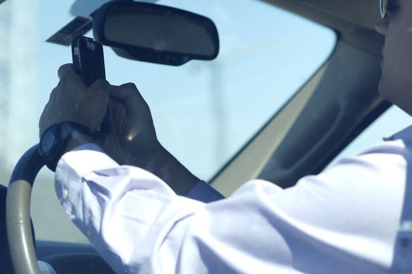 A man looks at his phone while driving down Woodall Rodgers Freeway in Dallas on July 16,...