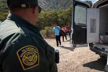 A Border Patrol agent leads a group of migrants seeking asylum towards a van to be...