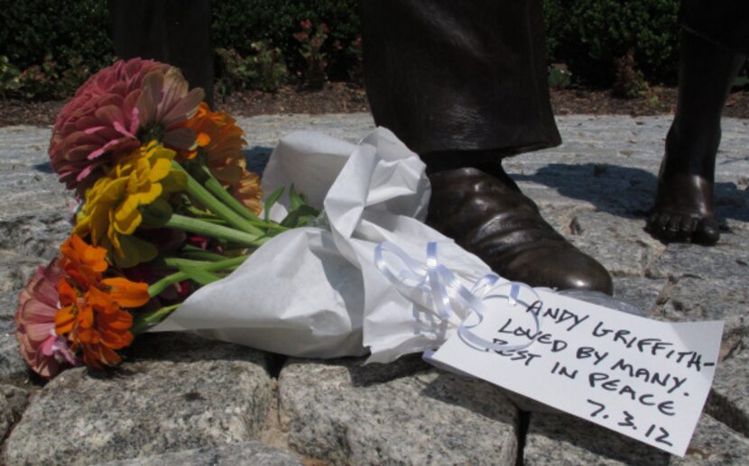 A bouquet of flowers at the foot of a statue of Andy Griffith at Pullen Park in Raleigh,...