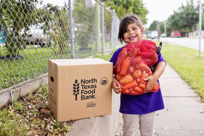 Young girl smiles and holds a net bag full of produce next to a cardboard box labeled North...
