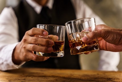 A close-up of two hands holding glasses filled with alcohol.