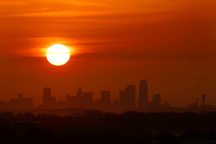 The sun rises behind high thin clouds over downtown Dallas on eclipse day, April 8, 2024.